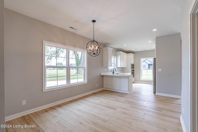 unfurnished dining area with a notable chandelier, light wood-type flooring, and sink