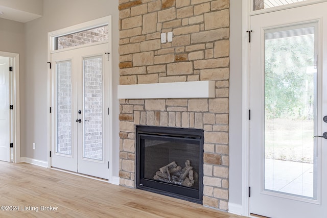 unfurnished living room featuring light hardwood / wood-style floors, plenty of natural light, french doors, and a stone fireplace