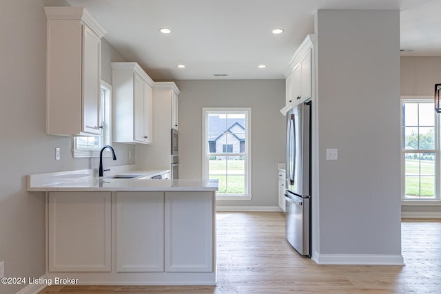 kitchen featuring light wood-type flooring, stainless steel fridge, white cabinetry, and sink