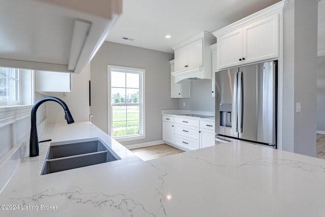 kitchen with light stone counters, stainless steel fridge with ice dispenser, sink, white cabinetry, and light hardwood / wood-style flooring