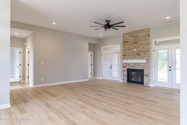 unfurnished living room with a fireplace, ceiling fan, french doors, and light hardwood / wood-style flooring