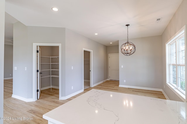 spare room with light wood-type flooring, a chandelier, and a healthy amount of sunlight