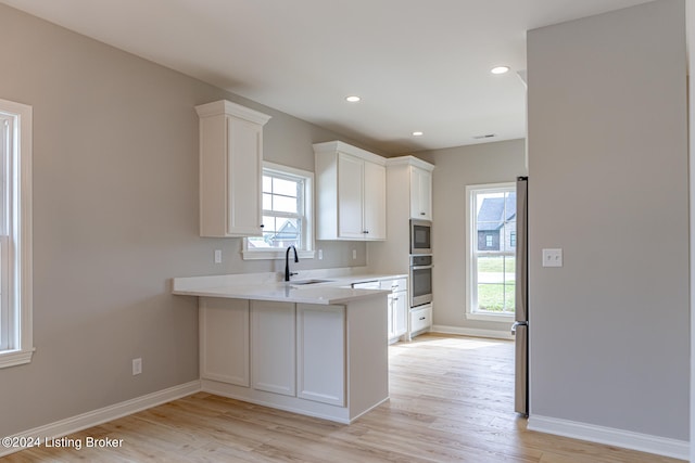 kitchen featuring white cabinets, light wood-type flooring, stainless steel fridge, and sink