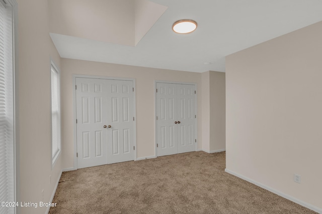 unfurnished bedroom with multiple windows, light carpet, and two closets