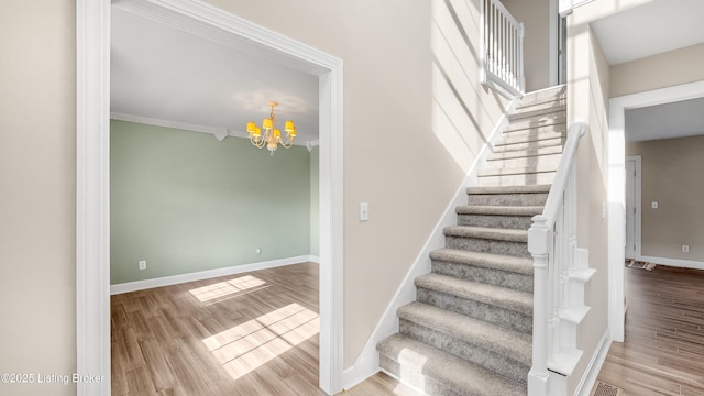 stairs featuring hardwood / wood-style floors, a notable chandelier, and ornamental molding