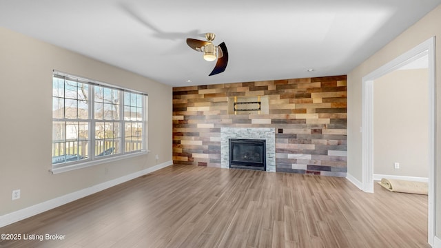 unfurnished living room with ceiling fan, wood walls, light wood-type flooring, and a fireplace