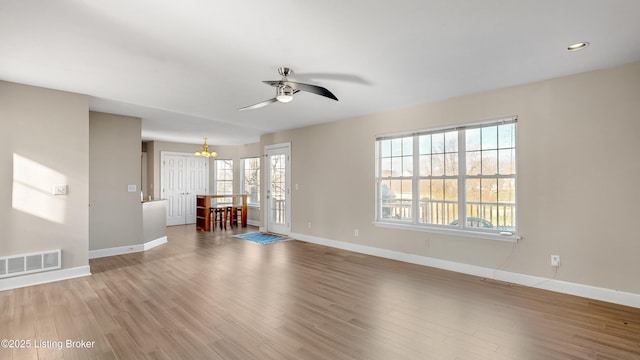 unfurnished living room featuring hardwood / wood-style flooring, ceiling fan with notable chandelier, and a wealth of natural light