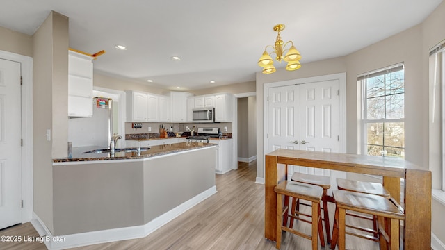 kitchen featuring kitchen peninsula, appliances with stainless steel finishes, dark stone counters, white cabinetry, and hanging light fixtures