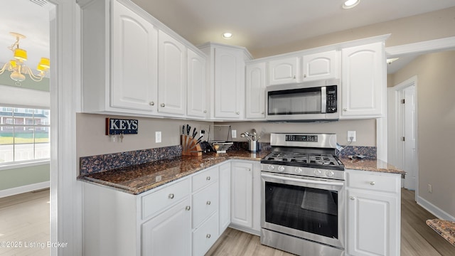 kitchen featuring white cabinets, appliances with stainless steel finishes, light hardwood / wood-style flooring, and dark stone countertops