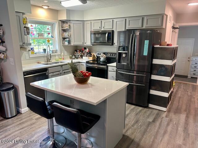 kitchen featuring black appliances, a kitchen island, sink, gray cabinetry, and light hardwood / wood-style floors