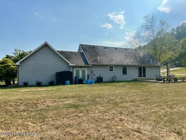 rear view of house with central AC unit and a lawn