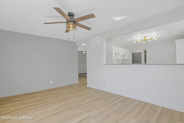 empty room with ceiling fan with notable chandelier, a textured ceiling, sink, and light hardwood / wood-style floors