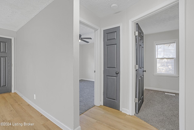 hallway with light wood-type flooring and a textured ceiling