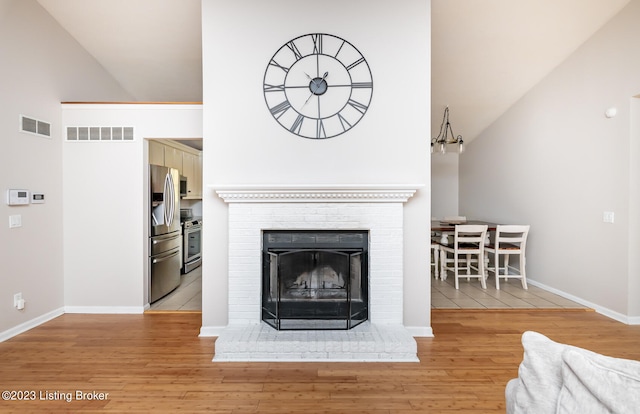 living room featuring light wood-type flooring, high vaulted ceiling, and a brick fireplace