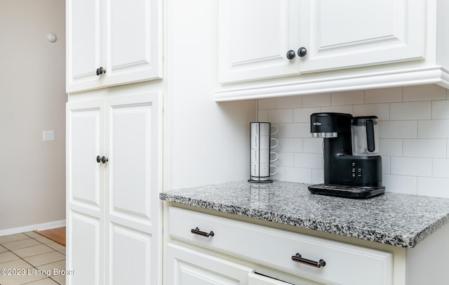 interior space featuring light tile patterned floors, light stone countertops, white cabinets, and tasteful backsplash