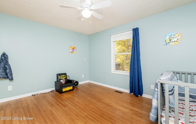 bedroom featuring a nursery area, wood-type flooring, ceiling fan, and a textured ceiling