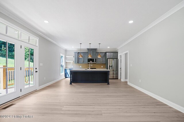 kitchen with light hardwood / wood-style flooring, appliances with stainless steel finishes, pendant lighting, decorative backsplash, and a center island with sink