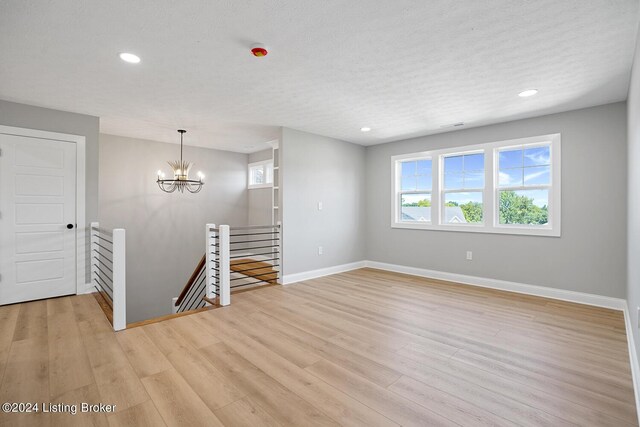 unfurnished room featuring light wood-type flooring, a textured ceiling, and a chandelier