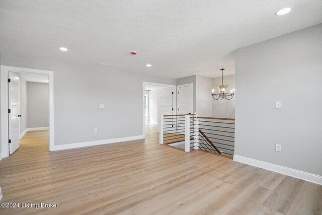 empty room featuring a notable chandelier and light hardwood / wood-style flooring