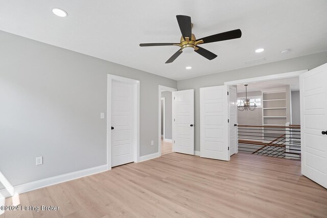 unfurnished bedroom featuring ceiling fan with notable chandelier and light hardwood / wood-style flooring