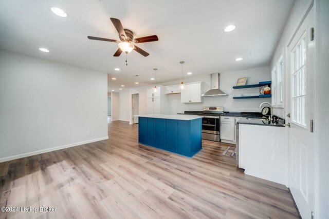 kitchen featuring wall chimney exhaust hood, stainless steel electric range oven, pendant lighting, light hardwood / wood-style floors, and white cabinetry