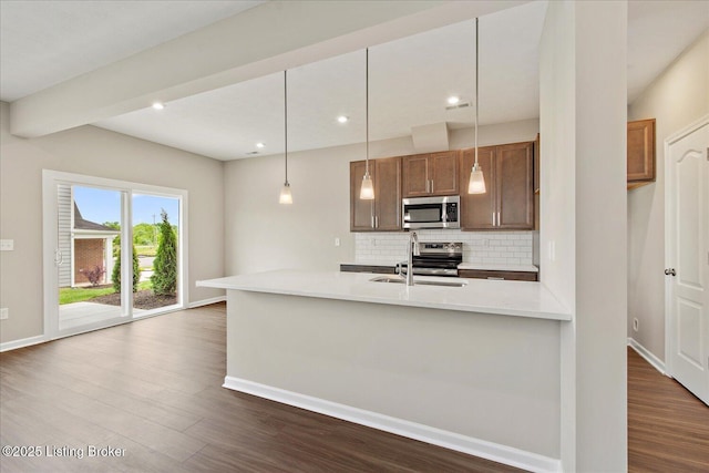 kitchen with appliances with stainless steel finishes, a sink, tasteful backsplash, dark wood-style floors, and baseboards
