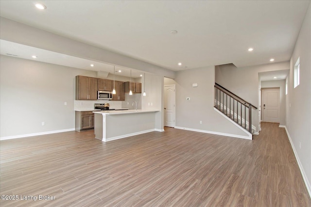 unfurnished living room featuring baseboards, light wood finished floors, recessed lighting, stairway, and a sink