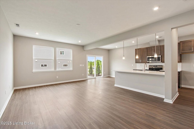 unfurnished living room with dark wood finished floors, baseboards, recessed lighting, and a sink