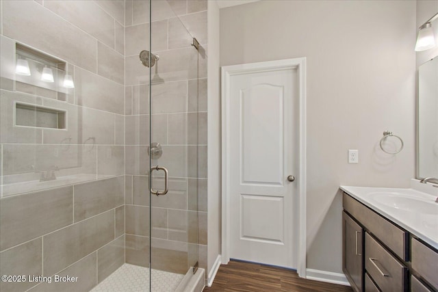 bathroom with a shower stall, vanity, wood finished floors, and baseboards