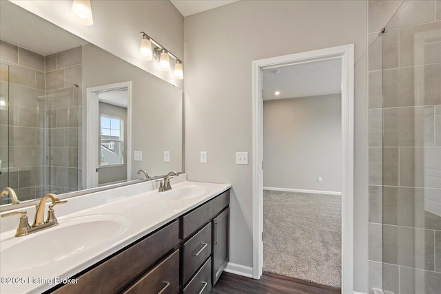 bathroom featuring a tile shower, double vanity, and baseboards