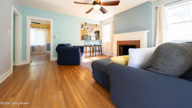 living room featuring plenty of natural light, ceiling fan, a brick fireplace, and light hardwood / wood-style floors