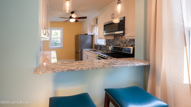 kitchen featuring a breakfast bar area, stainless steel appliances, decorative backsplash, ceiling fan, and white cabinets