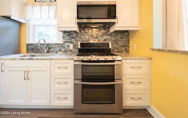 kitchen with light stone countertops, dark hardwood / wood-style flooring, appliances with stainless steel finishes, sink, and decorative backsplash