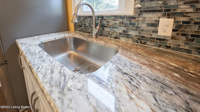 details featuring tasteful backsplash, sink, and light stone countertops