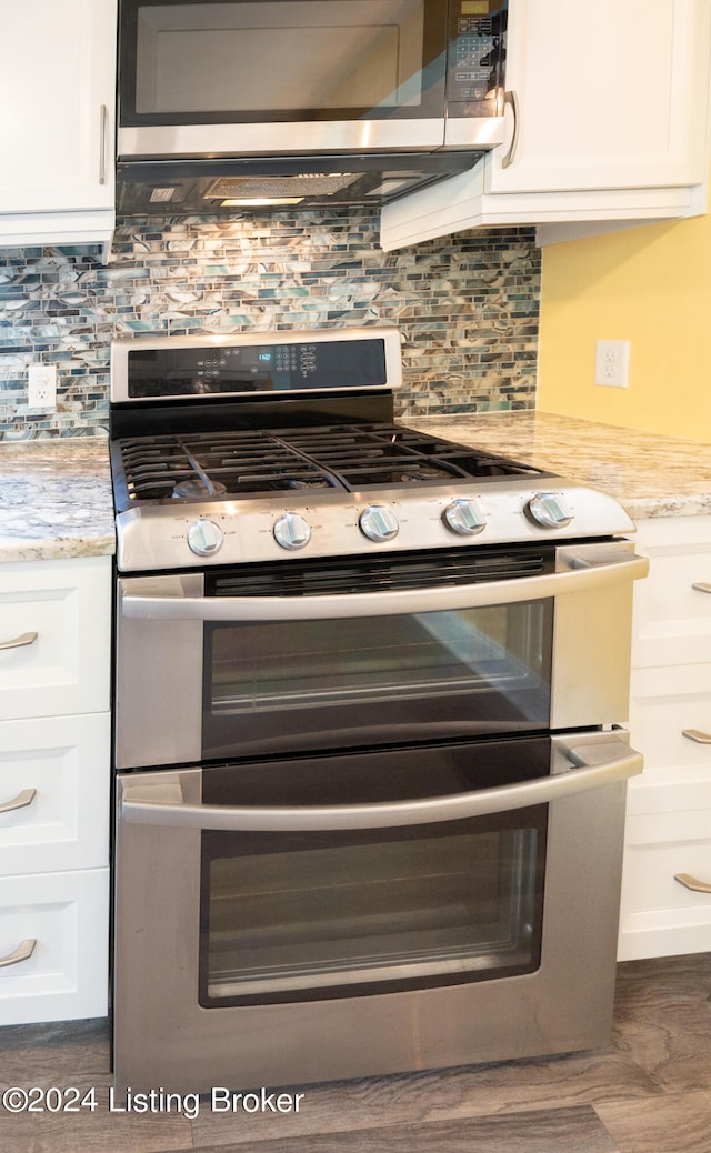 kitchen with white cabinets, appliances with stainless steel finishes, light stone counters, and tasteful backsplash