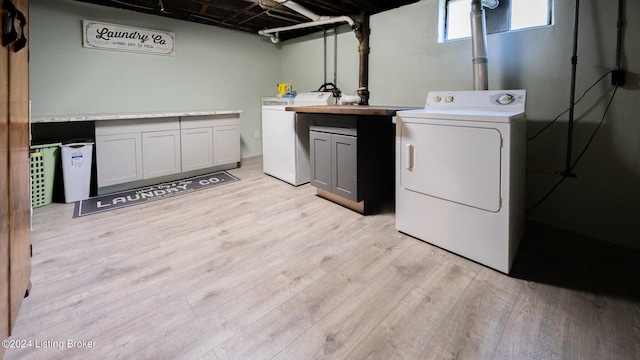 clothes washing area featuring light wood-type flooring, washing machine and clothes dryer, and cabinets