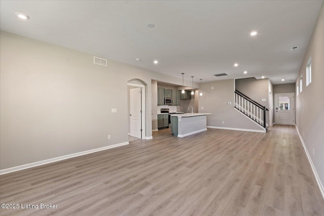 196 Harvest Moon Ct Unit 219A, Shepherdsville, KY 40165 - unfurnished living room with light wood-style flooring, baseboards, a sink, arched walkways, and stairway