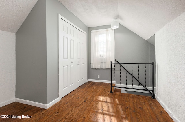 bonus room with lofted ceiling, hardwood / wood-style flooring, and a textured ceiling