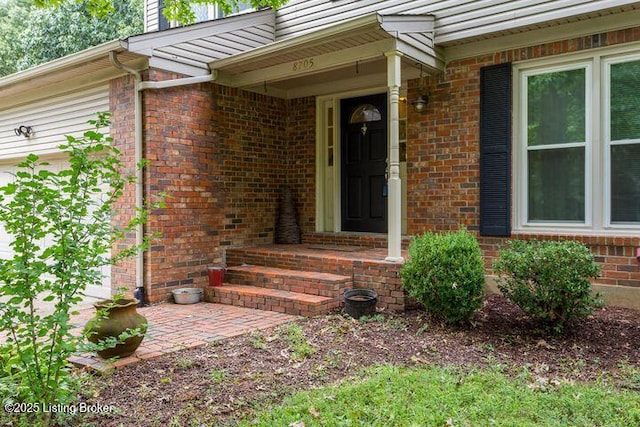 property entrance with a patio area, brick siding, and an attached garage