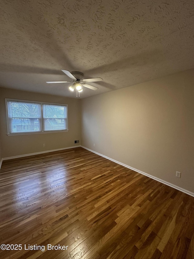 empty room featuring a ceiling fan, dark wood finished floors, a textured ceiling, and baseboards