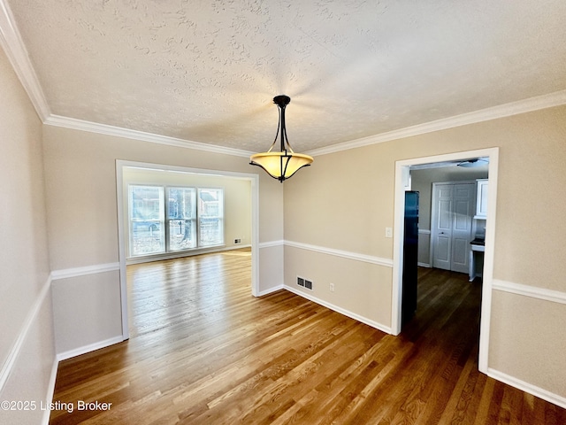 unfurnished dining area featuring dark wood-type flooring, visible vents, crown molding, and a textured ceiling