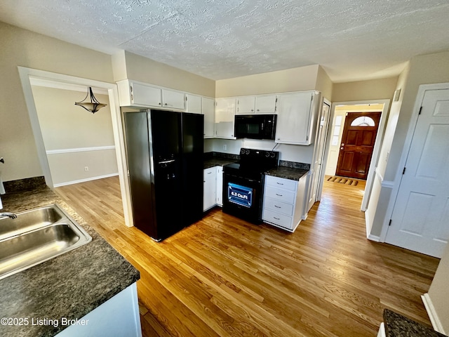 kitchen with a textured ceiling, baseboards, light wood-style floors, white cabinets, and black appliances