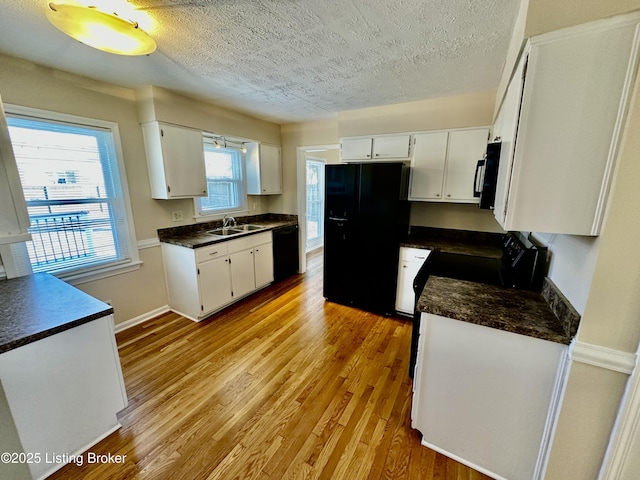 kitchen featuring light wood finished floors, dark countertops, white cabinets, a sink, and black appliances