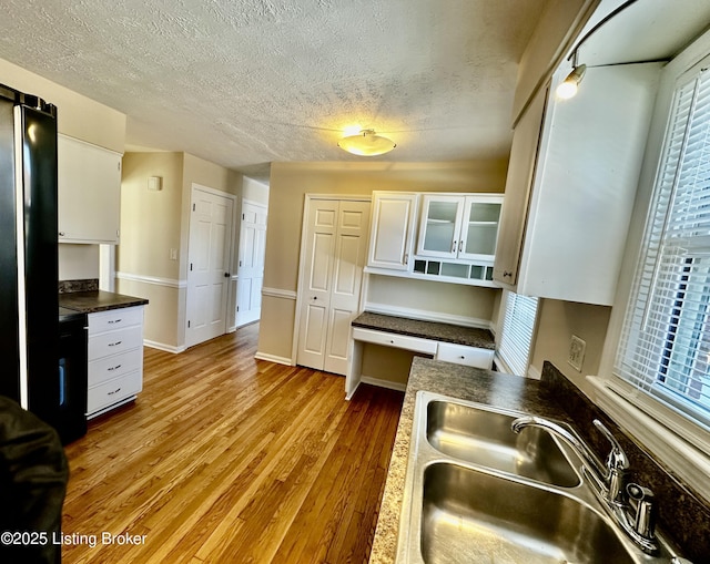 kitchen featuring light wood-style flooring, a sink, white cabinets, built in desk, and glass insert cabinets