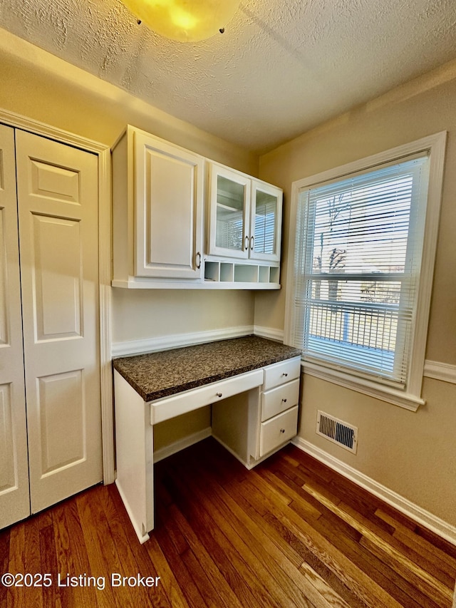 unfurnished office with baseboards, visible vents, dark wood-type flooring, a textured ceiling, and built in desk