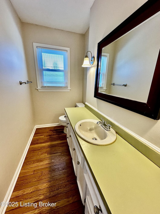 half bathroom with baseboards, vanity, toilet, and wood finished floors