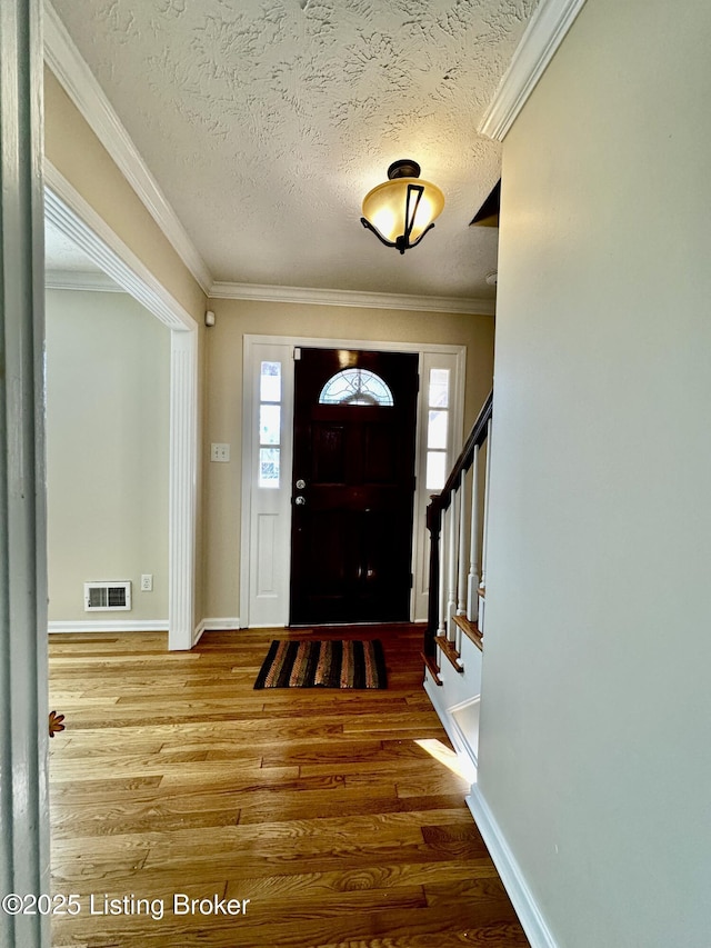 entrance foyer with ornamental molding, visible vents, a textured ceiling, and wood finished floors