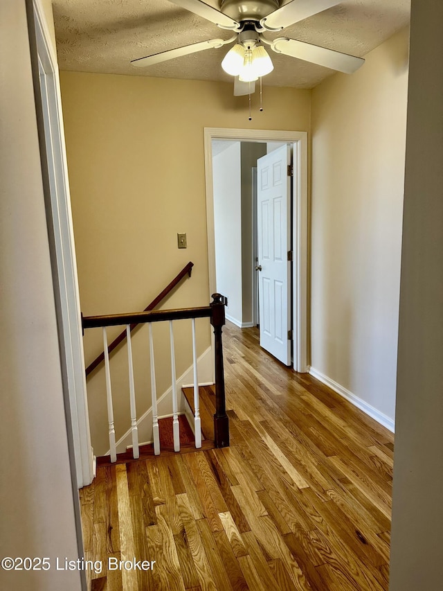 staircase with a textured ceiling, ceiling fan, wood finished floors, and baseboards