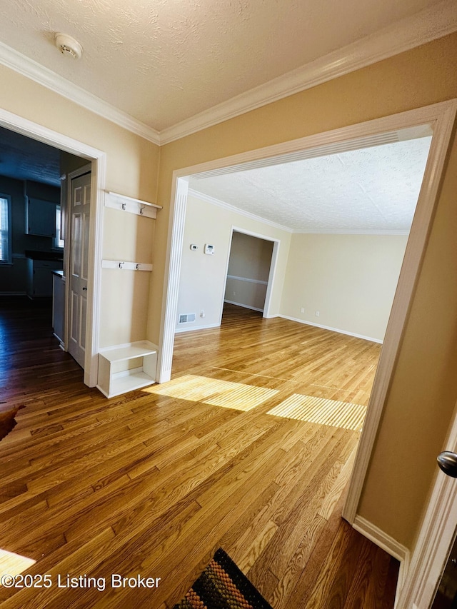 unfurnished room featuring visible vents, ornamental molding, a textured ceiling, wood finished floors, and baseboards