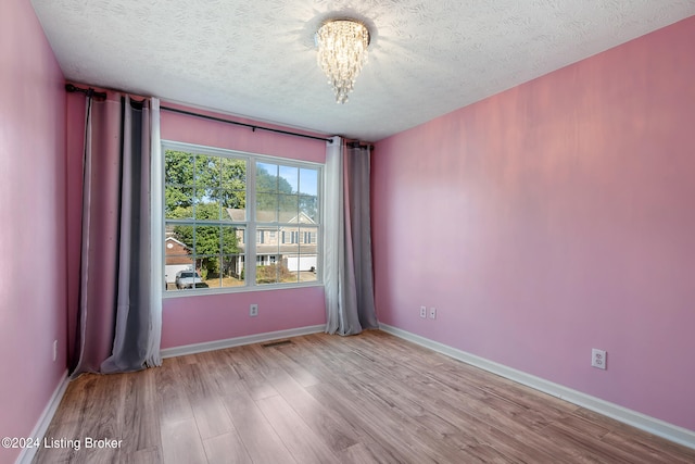 unfurnished room featuring a textured ceiling, light hardwood / wood-style flooring, and a notable chandelier